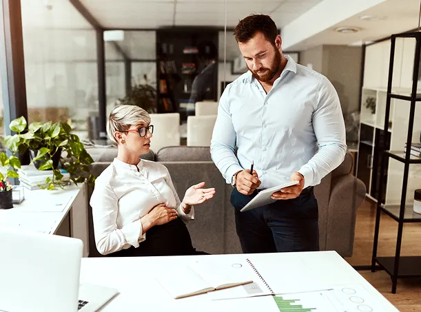 A photo of two coworkers discussing work in an office.