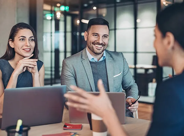 Three people having a friendly meeting at a table with laptops